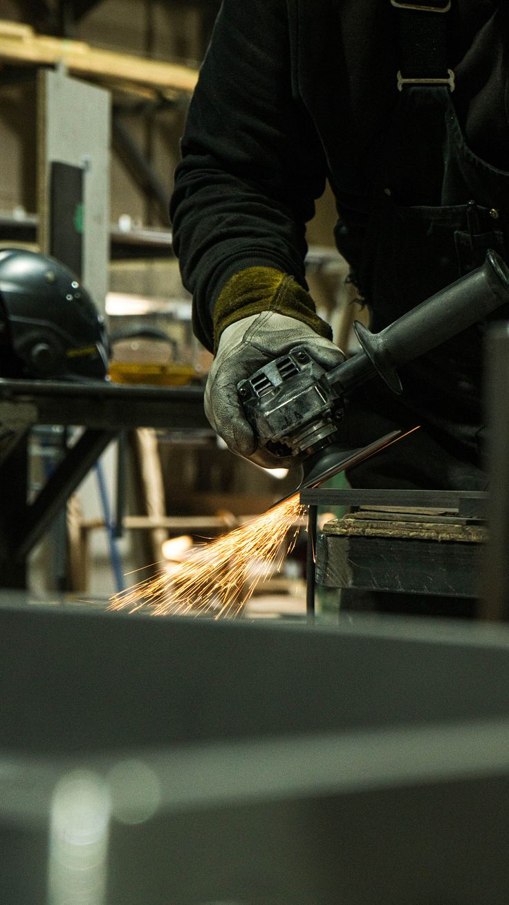 Metalworker using an angle grinder in a fabrication shop, with sparks
